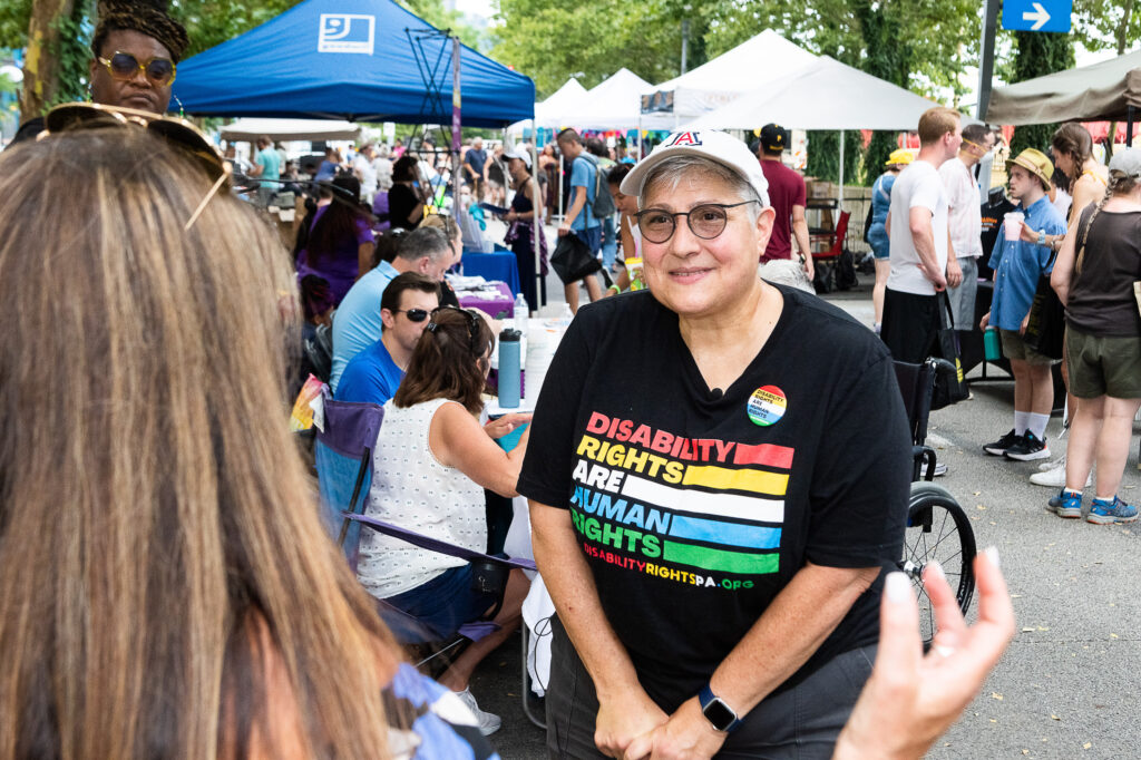 A figure wearing a black t-shirt that says "Disability Rights are Human Rights" smiles.